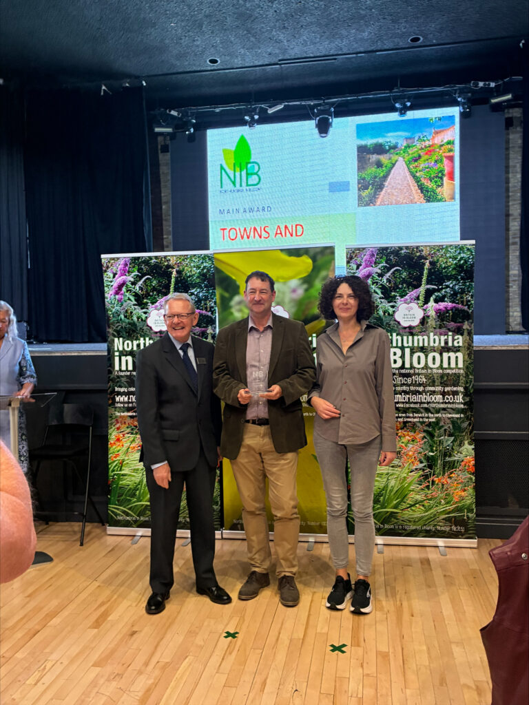 Mayor of Bishop Auckland, Councillor Michael Siddle with Volunteer Agnes Wasiluk a volunteer representative of the Greener Together Group receiving the award from Rae Beckwith, Senior RHS Britain In Bloom UK Finals Judge and Chelsea Flower Show Judge.